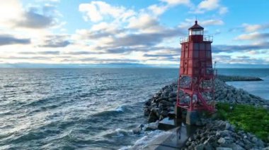 Racine Dalgakıran Deniz Feneri 'nin Wisconsin' de gündoğumunda sakin bir hava manzarası. Canlı kırmızı deniz feneri, Michigan Gölü ve kayalıklarla çevrili, altın bir gökyüzüne karşı dimdik ayakta duruyor.