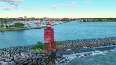 Hava Sabit Çekimi: Michigan Gölü 'ndeki Racine Breakwater Deniz Feneri' nin sakin gün doğumu görüntüsü. Kırmızı deniz feneri kayalık bir dalgakıranda duruyor. Racines marinası ve arka planda ufuk çizgisi var.