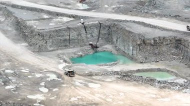 Aerial Tilt Shot: Fort Wayne, Indiana 'da geniş çaplı bir taş ocağı, büyük çöp kamyonları ve kazıcıların çalıştığı yer. Engebeli arazi, kayalık duvarlar ve turkuaz havuzlar sanayi ve doğayı ön plana çıkarıyor