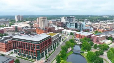 Kalamazoo, Michigan şehir merkezinin havadan çekilmiş görüntüleri, modern ve tarihi mimari, yemyeşil parklar ve sakin, bulutlu gökyüzü altında sakin su yolları karışımı sergileniyor. Hayat dolu ve...