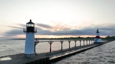 Michigan 'daki ikonik St. Joseph deniz fenerlerinin üzerinde sakin bir güneşin doğuşunun havadan çekilmiş görüntüsü. Siyah ve kırmızı çatı yapıları durgun göldeki altın renkleri yansıtan bir rıhtımda dimdik duruyorlar.