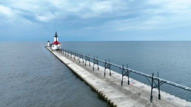 St. Joseph Deniz Feneri 'nin sakin manzarası ve Michigan' daki iskele. Michigan Gölü 'nün yanında kırmızı çatılı deniz feneri duruyor. Etrafı sakin sular ve bulutlu bir gökyüzü ile çevrili. Ziyaretçiler geziniyor