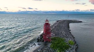 Ark Shot: Wisconsin 'de gün doğumunda Racine Breakwater Deniz Feneri' nin hava görüntüsü. Kırmızı deniz feneri Michigan Gölü 'nün sakin sularıyla çevrili kayalık bir dalgakıranın üzerinde belirgin bir şekilde duruyor.