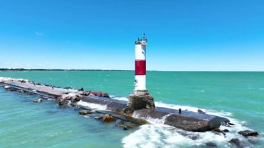Michigan Gölü 'ndeki Kenosha Deniz Feneri' nin havadan görüntüsü. Canlı mavi sular ve açık gökyüzü kontrastı kayalık iskeledeki kırmızı çizgili fenerle. Tepeye tünemiş kuşlar sakin kıyı manzarasına eklenir..