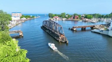 Havadan uçarak Michigan 'daki St. Joseph Swing Köprüsü' nün yemyeşil ve dingin mavi sularla çevrili büyüleyici görüntüsü. Bir tekne köprüye doğru ilerliyor, bu resmi vurguluyor.