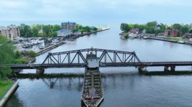 Hava Arc Shot: Michigan 'daki St. Joseph Swing Köprüsü' nün çarpıcı görüntüsü, dingin su yolları, canlı yeşillikler, kıyı binaları ve parlak gündüz gökyüzü altında rıhtımlı botları olan marinaları vurguluyor