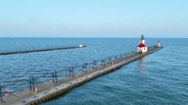 Güneş doğarken Michigan 'daki St. Joseph deniz fenerinin kırmızı çatısını ve beyaz cephesini gösteren hava yayı görüntüsü. Michigan Gölü 'nün sakin suları ve uzun iskele huzur dolu sabahı daha da güçlendiriyor.