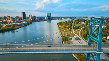 Ohio, Toledo üzerinde altın saat Maumee Nehri 'ni kaplayan Anthony Wayne Köprüsü' nü yakalıyor. Bu hava manzarası şehir canlılığını ve şehir hayatı ile dingin yeşil alanlar arasındaki dengeyi vurgular..