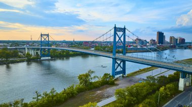 Toledo Ohio 'daki Maumee Nehri' nin üzerindeki ikonik mavi Anthony Wayne Köprüsü 'nün hava görüntüsü çarpıcı bir günbatımı şehir manzarası ile kentsel bağlantı ve sükuneti vurguluyor..