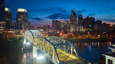 Nashville üzerindeki Alacakaranlık: Aydınlanmış John Seigenthaler yaya köprüsü Cumberland Nehri boyunca uzanır ve tarihi cazibeyi modern ufuk çizgisine bağlar. Şehir merkezinde canlı bir Tennessee manzarası.