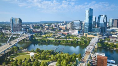 Nashville 'in hava manzarasında canlı şehir silueti, Cumberland Nehri üzerindeki ikonik köprüler ve yemyeşil parklar bulunur. Modern mimari ve doğal güzelliğin ahenkli bir karışımını deneyimleyin..