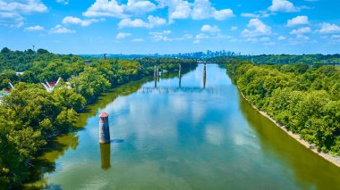 Tennessee Nehri 'nden yükselen Nashville deniz feneri Omohundro Su İşleri Işığı' nın havadan görünüşü, bereketli ormanlar, doğayı ve kentsel kenti harmanlayan mavi gökyüzünün altında bir tren köprüsü ve şehir silüeti ile buluşuyor.