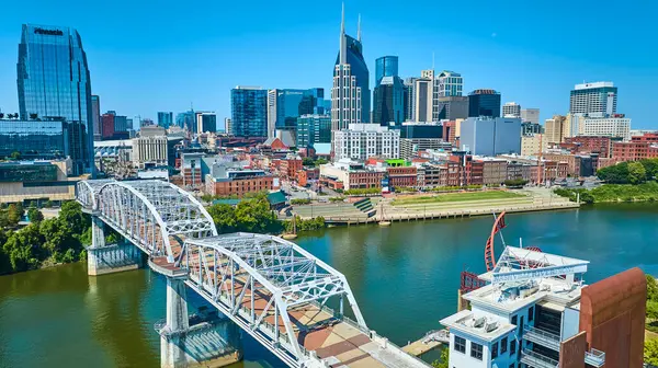 Nashville şehir merkezinin nefes kesici hava manzarası, ikonik ATT Binası 'nı ve John Seigenthaler Pedestrian Köprüsü' nü açık mavi gökyüzüne karşı gösteriyor. Nehir ve şehir siluetini keşfedin..