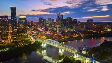 Nashville 'in havadan görünüşü alacakaranlıkta ufuk çizgisini aydınlattı. ATT Binası, John Seigenthaler Yaya Köprüsü 'nün Cumberland Nehri' nin aşağısındaki ışıkları yansıttığı yüksek kuleler..