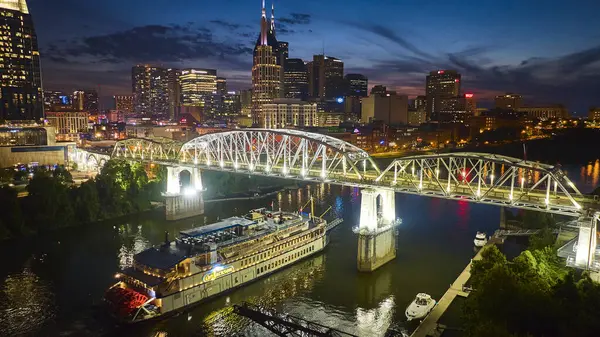 stock image Vibrant aerial view of downtown Nashville at night: the illuminated skyline including the iconic ATT Building, the historic General Jackson riverboat, and the John Seigenthaler Pedestrian Bridge.