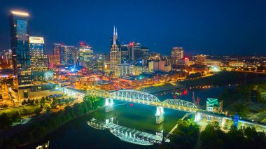 Nashville 'in mavi saatindeki hava manzarası ikonik Batman Binası' nı ve Cumberland Nehri üzerindeki aydınlanmış John Seigenthaler Yaya Köprüsü 'nü aydınlatıyor.