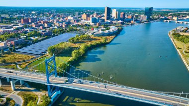 Toledo, Ohio 'nun canlı hava manzarası Maumee Nehri üzerindeki ikonik mavi Anthony Wayne Köprüsü' nü gösteriyor. Şehir merkezi ufuk çizgisi ve güneş panelleri kentsel büyüme ve sürdürülebilirliği yansıtıyor.