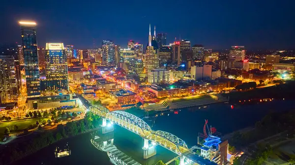 stock image Vibrant Nashville skyline at night featuring the iconic Batman Building and John Seigenthaler Pedestrian Bridge. The city lights reflect on the Cumberland River, capturing urban energy and growth.