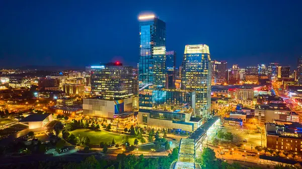 stock image Experience the vibrant Night Time aerial view of Nashville skyline, featuring the illuminated downtown and iconic John Seigenthale Pedestrian Bridge, set against the serene riverfront and lush green