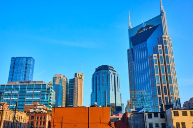 Açık mavi gökyüzünün altında canlı bir Nashville silueti. Sembolik ATT Binası, Bölge Merkezi ve modern gökdelenler. Bu görüntü, tarihi cazibe ve kentsel gelişimin karışımını yakalar..