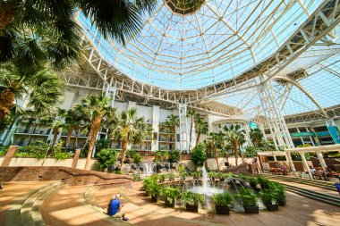 Discover tranquility at Gaylord Opryland in Nashville. This stunning atrium with a glass ceiling bathes lush gardens and a central fountain in natural light, offering a perfect urban retreat.