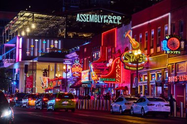 Canlı neon ışıklar Nashville, Tennessee 'de Broadway' i aydınlatıyor, hareketli gece hayatını gözler önüne seriyor. Arabalar, taksiler ve kalabalık bu ikonik eğlence bölgesinin canlı atmosferini yansıtıyor..