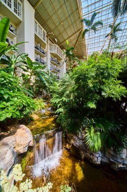 Escape to tranquility at Gaylord Opryland in Nashville. Experience the lush indoor garden featuring a cascading waterfall amidst vibrant tropical plants under a stunning glass atrium.
