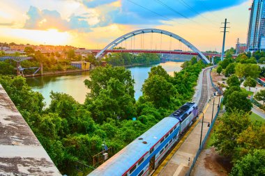 Günbatımı treni, Nashville 'de ikonik Koreli Gaziler Anıtı Köprüsü' nün altından gökyüzüne karşı durduğu yemyeşil bir nehir boyunca ilerliyor. Doğa ve şehir güzelliğinin mükemmel bir karışımı..