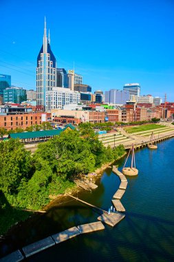 Muhteşem Nashville silueti simgesel Batman Binası Cumberland Nehri boyunca yemyeşil alanlar ve berrak mavi gökyüzü altında tarihi ve modern mimarinin canlı bir karışımı..