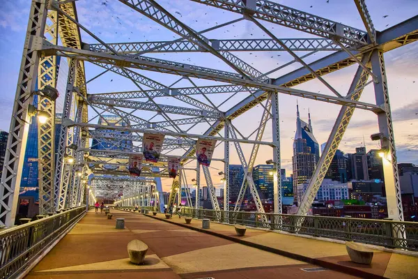 stock image Stroll the stunning John Seigenthaler Pedestrian Bridge at blue hour in Nashville. Enjoy the warm glow of city lights and witness the iconic skyline vistas with the famous Batman Building in view.