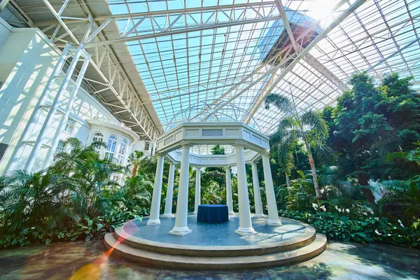 stock image Elegant white gazebo amidst lush tropical plants in Gaylord Opryland, Nashville. Sunlight streams through a glass ceiling creating a serene and inviting atmosphere perfect for events or relaxation.