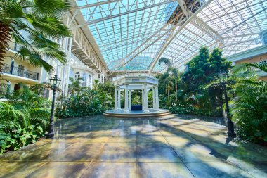 Experience tranquil elegance at the Gaylord Opryland grand conservatory. Marvel at the classical white gazebo amid lush greenery under a sunlit glass ceiling. Perfect for a serene retreat.