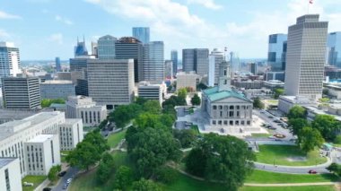 Havadan İzleme Çekimi: Tarihin ve modernliğin harmanlanmış Nashvilles 'i keşfedin Tennessee Eyaleti Kongre Binası, şehir dinamik ufuk çizgisi ve mavi gökyüzü tarafından çerçevelenmiş, yemyeşil yemyeşil ortamda duruyor..