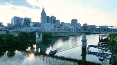 Nashville 'in ikonik John Seigenthaler Pedestrian Köprüsü' nün altın saatinde havadan görünüşünü sergiliyor. Yüzen bir tekne, kentsel ve doğanın karışımını vurguluyor.