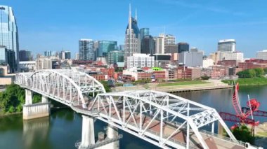 Aerial Fly Through Forward: Experience Nashvilles, simgesel Batman Binası, John Seigenthaler Yayalar Köprüsü ve Cumberland Nehri boyunca yemyeşil nehir kıyısı ile canlı bir ufuk çizgisi.