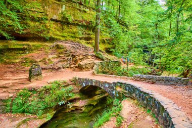 Explore the scenic beauty of Hocking Hills, Ohio. Discover serenity on the Old Mans Cave Trail as you cross the historic stone bridge amid lush fall foliage and tranquil woodland surroundings. clipart