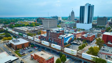 Fort Wayne, Indiana 'nın havadan görünüşü: Bir yük treni tarihi ve modern mimaride dokuma yapıyor, kentsel canlılık sergiliyor. Renkli duvar resmi ve ufuk çizgisi sanatsal ve ticari cazibe katıyor..