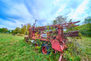 Rusted water well drill overgrown with weeds stands silent in a rural Ohio field. Nature reclaims the forgotten machine under the soft afternoon sky, capturing a tale of industrial decay and renewal. clipart