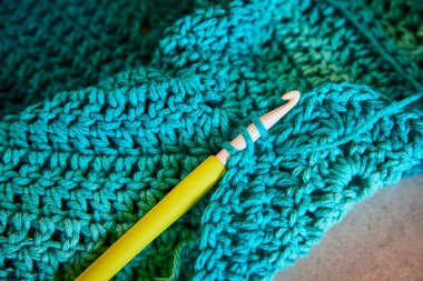 Fort Wayne, Indiana 'daki bir tığ işi projesinin yakın çekimi. Canlı mavi iplik ve yeşil kanca, rahat ve sıcak bir dokunuşla zanaat sanatını sergileyen, karmaşık bir desen oluşturur. DIY için mükemmel.