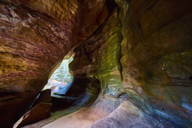 Hocking Hills Ohio 'daki Rock House mağarasının doğal güzelliklerini keşfedin. Güneş ışığı desenli duvarlarda dans eder. Toprak rengini gösterir. Macera ve doğa meraklıları için mükemmel manzaralı güzellik..