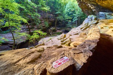 Explore the serene beauty of Hocking Hills, Ohio, with lush forests and rocky trails. Discover the Old Mans Cave Trail while respecting conservation with the No Trail Do Not Cross sign in view. clipart