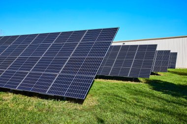 Solar panels bask in the sun in Waterloo, Indiana, exemplifying clean energy and sustainability. A bright blue sky frames this modern eco-friendly technology against an industrial backdrop. clipart