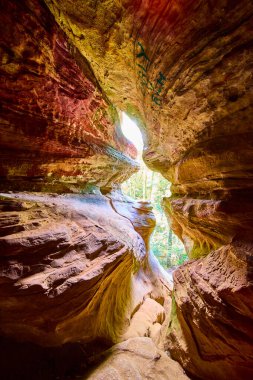 Hocking Hills, Ohio 'daki büyüleyici Kaya Evi mağarasını keşfedin. Güneş ışığı canlı kumtaşı üzerinde dans eder, sizi bu doğal harikanın zengin dokularını ve toprak renklerini keşfetmeye davet eder..