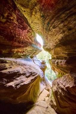 Explore the enchanting Rock House cave in Hocking Hills, Ohio. Sunlight dances on vibrant sandstone, inviting you to discover the rich textures and earthy hues of this natural wonder. clipart