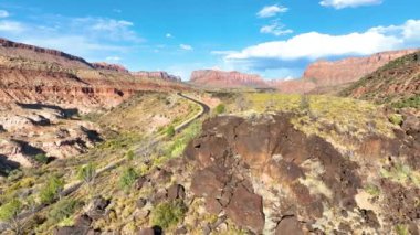 Zion Ulusal Parkı 'ndaki Kolob Kanyonu üzerinde havadan izleme görüntüleri. Berrak mavi gökyüzü altında çarpıcı kırmızı kaya oluşumları arasında dönen bir yol yılanı, keşif ve maceraya davetiye çıkarıyor..