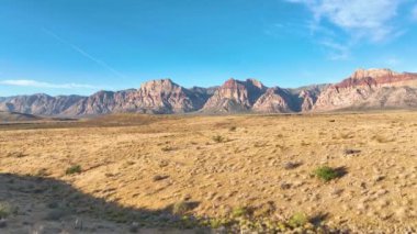 Havadan Uç: Las Vegas yakınlarındaki Red Rock Kanyonu üzerinde süzül, orada altın saat ışığı görkemli kırmızı kaya oluşumları ve geniş çöl manzarası sıcak, sakin bir parıltı.