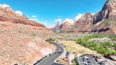 Havadan Kuruluş Çekimi: Springdale, Utah 'taki çarpıcı Zion Ulusal Parkı girişi. Dramatik kırmızı kaya oluşumları, açık mavi gökyüzünün altındaki yemyeşil vadileri çevreleyerek, doğanın ihtişamını vurguluyor..