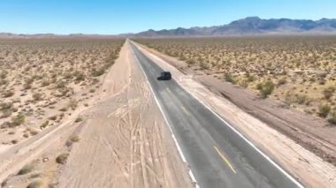 Aerial Fly Through Forward: Boulder City, Nevada 'da terk edilmiş bir yol boyunca yolculuk. Uçsuz bucaksız çöl arazisinde tek başına yolculuk eden bir araç, açık bir şekilde özgürlük ve keşif hissi uyandırıyor.