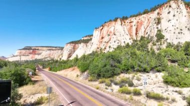 Zion Ulusal Parkı 'nın doğu girişinin havadan çekilmiş görüntüsü çarpıcı kırmızı ve beyaz uçurumlar, açık mavi gökyüzü ve dolambaçlı bir yol gösteriyor. Utahlar' ın doğal harikalarında macera ve keşiflere davetiye çıkarıyor.