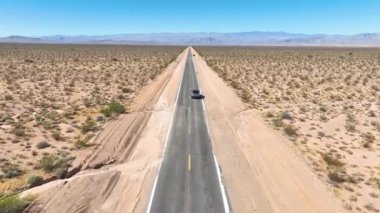 Havadan Uçarak İlerlemek: Nevada çölünün uçsuz bucaksız ıssızlığını, uzak dağlar ve parlak mavi gökyüzü tarafından çerçevelenmiş sonsuz bir yol boyunca tek başına seyahat eden bir araba olarak tecrübe edin. Bir özgürlük sahnesi.